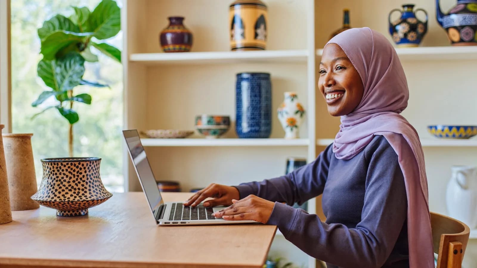 A smiling shop owner working on a laptop in her bright ceramics boutique